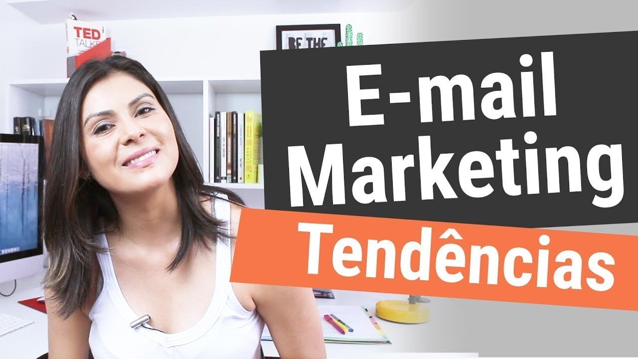 Uma pessoa com longos cabelos escuros, vestindo uma blusa branca, sorri enquanto está sentada em uma mesa. Atrás deles estão estantes com vários livros e um computador. O texto grande na imagem diz “Tendências de email marketing 2024. | Morabeza Marketing